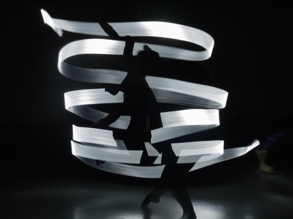 A dancer's silhouette is illuminated by ribbons of bright white light.