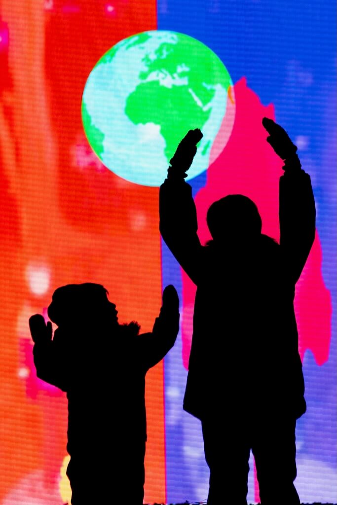 Children's silhuoettes stand in from of a bright screen displaying planet Earth and bright swathes of blue and orange.