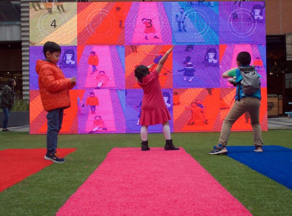 3 kids create different shapes to pose for the camera on a timer.