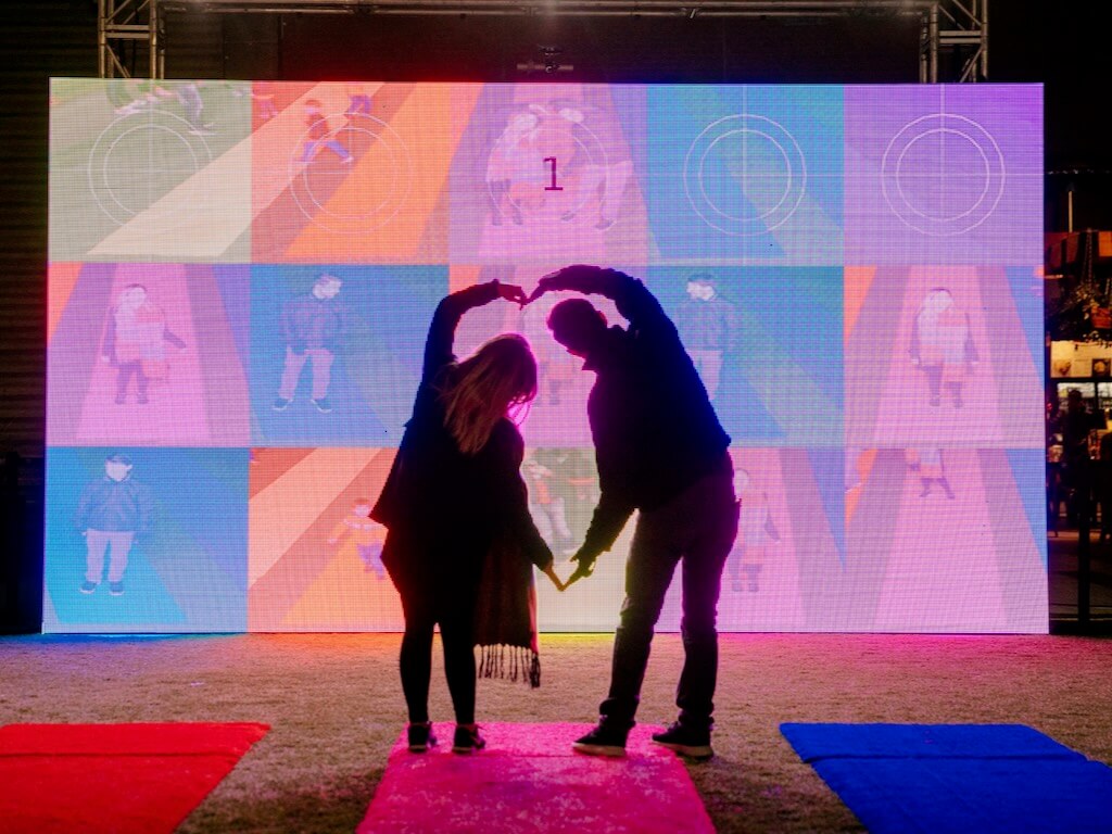 A couple poses together to form a love heart, interacting with Colour Me Beautiful to create fun images.