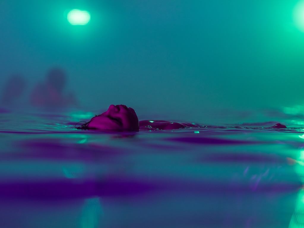 A woman floats across a pool, both the water and the air are exquisite shades of teal and turquoise.