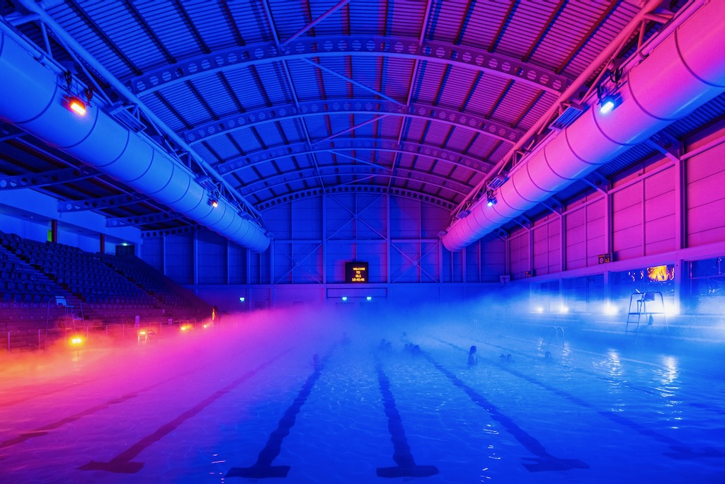 Strategically placed pink and blue lights illuminate the inside of an Olympic size swimming pool.