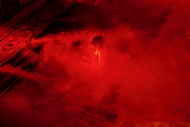A woman emerges through red mist as she exits a swimming pool.