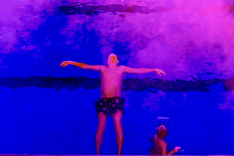 A man floats serenely in a bright blue as pink mist begins to roll across the water towards him.