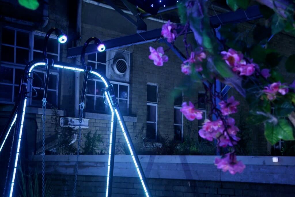 The LightBug swing set is illuminated next to beautiful pink flowers.