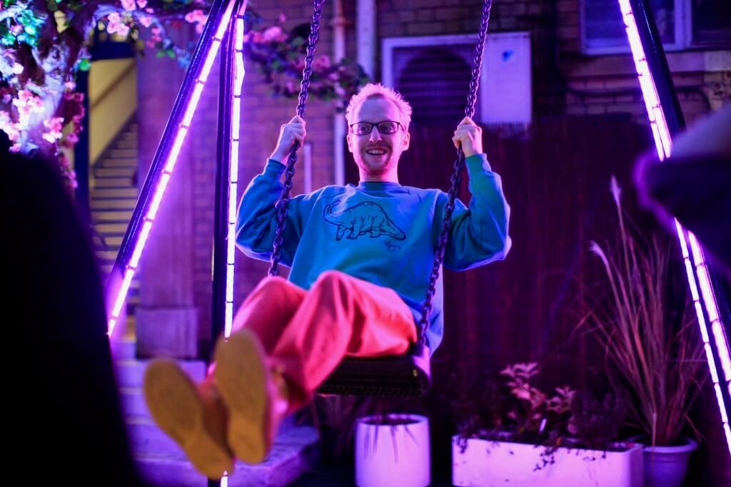 Ablaze in pink light, a man playfully swings on the LightBug swing set.