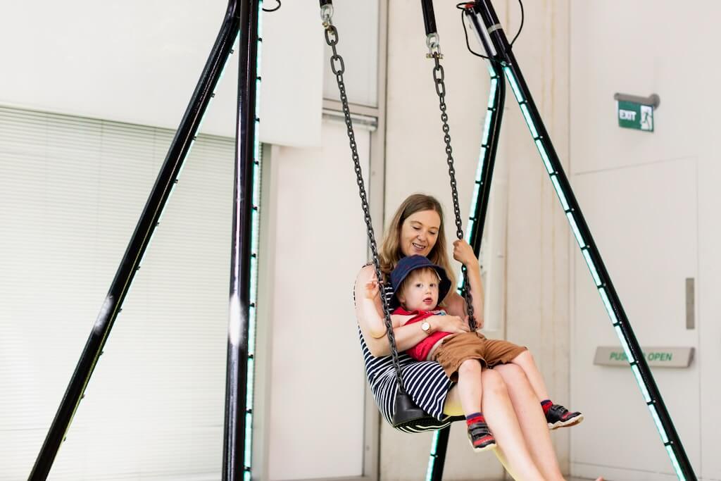 A mother and her child happily swing on a light activating swing set.