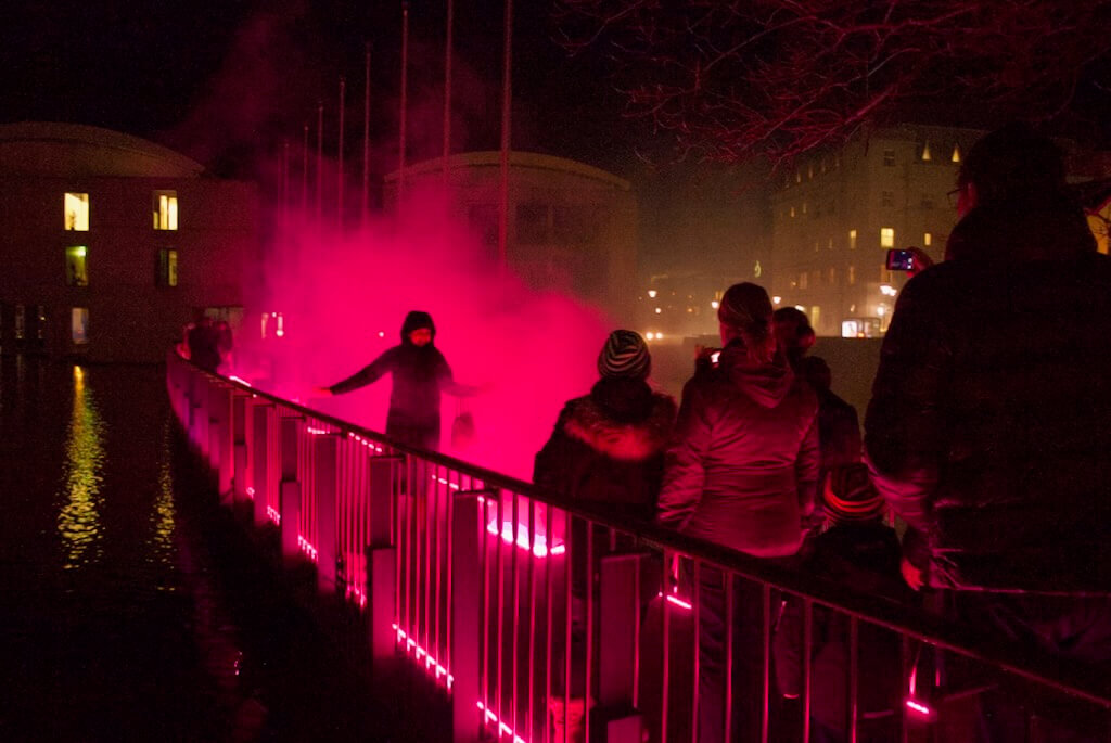 Families smile and laugh as they experience walking through clouds of pink light.