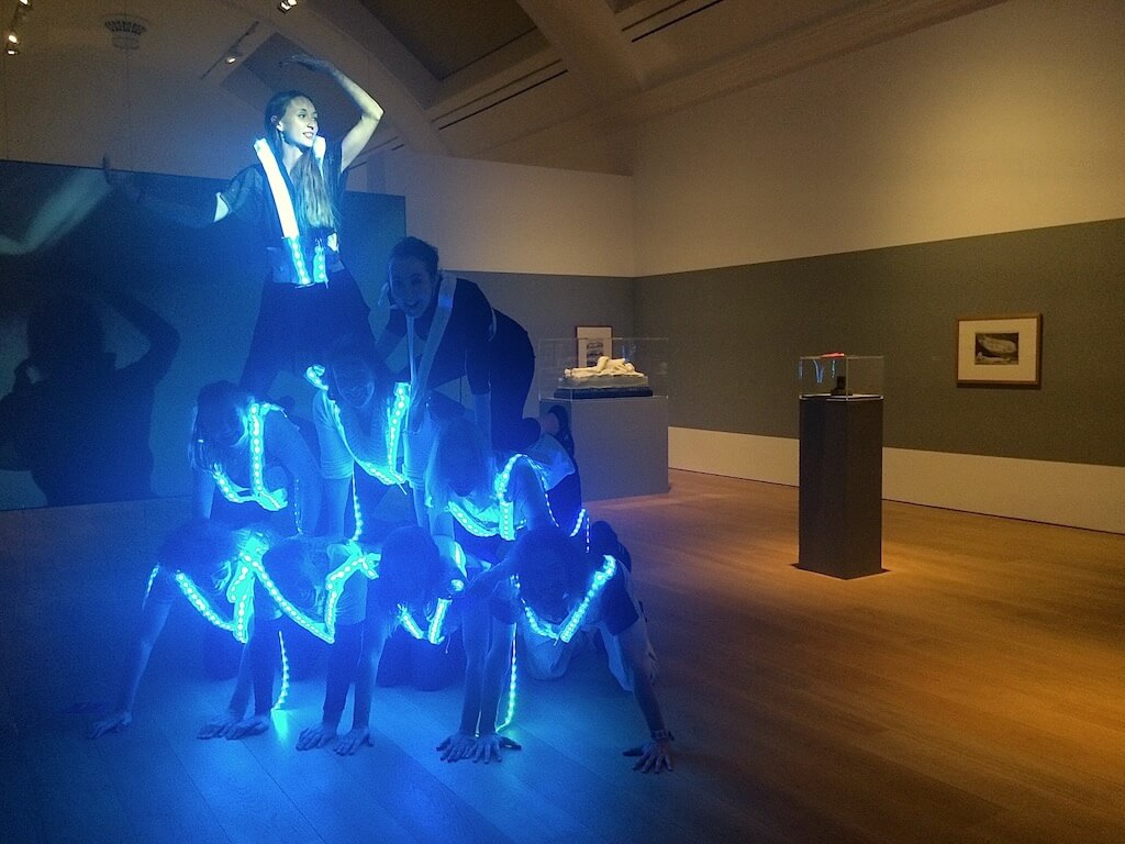 9 game players create a human pyramid of blue light.