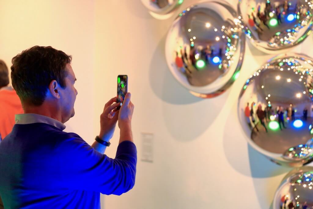 A man takes a photo of silver reflective orbs.