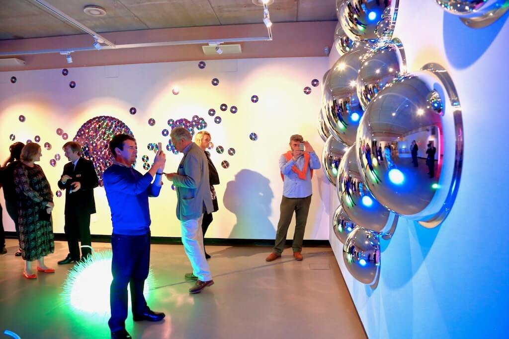 A room of excited visitors marvel at Tine's exhibition.