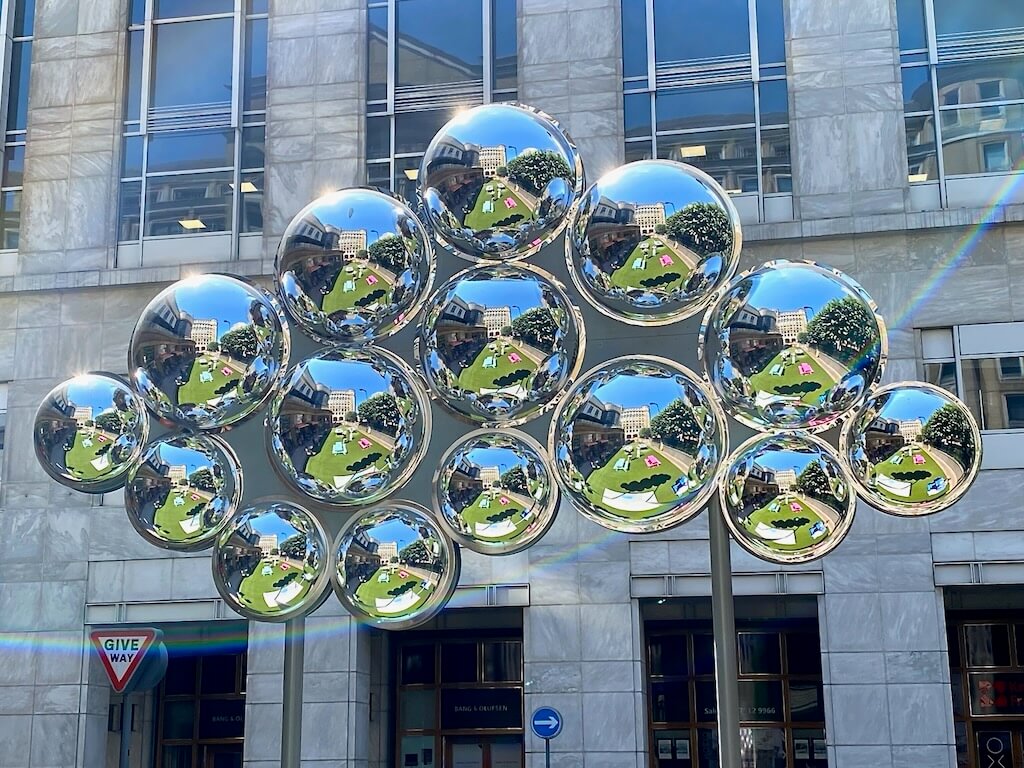 A public park is reflected by silver orbs arranged in the shape of a cloud.