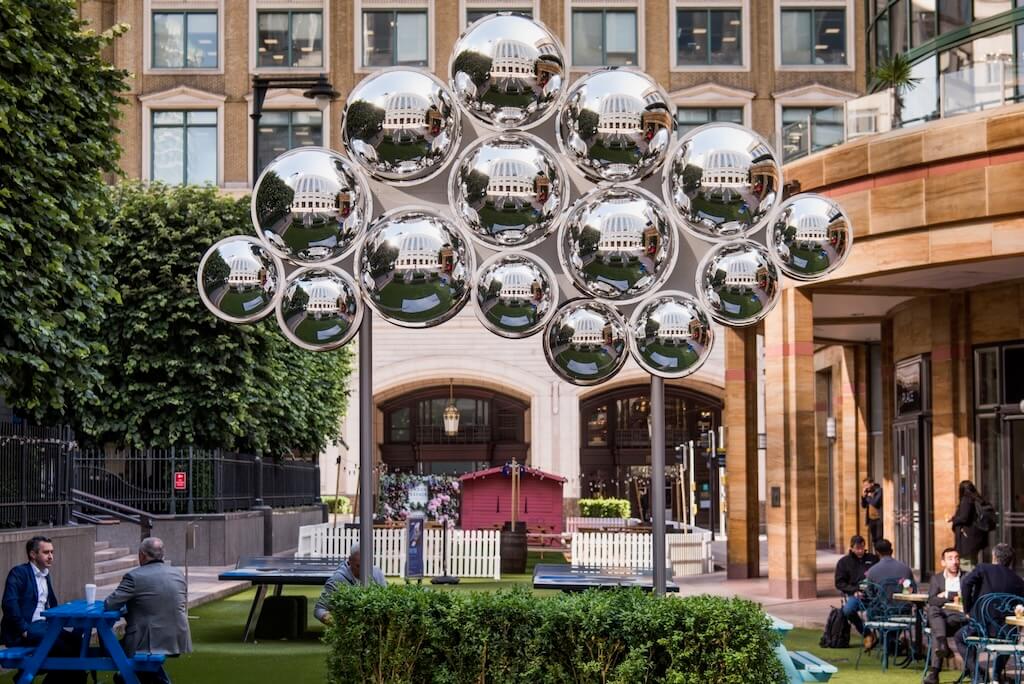 A giant cloud sculpture created with reflective silver orbs stands tall above a public space.