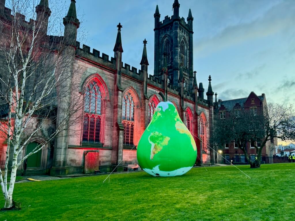The ginormous pear sits in front of a cathedral illuminated with red light.
