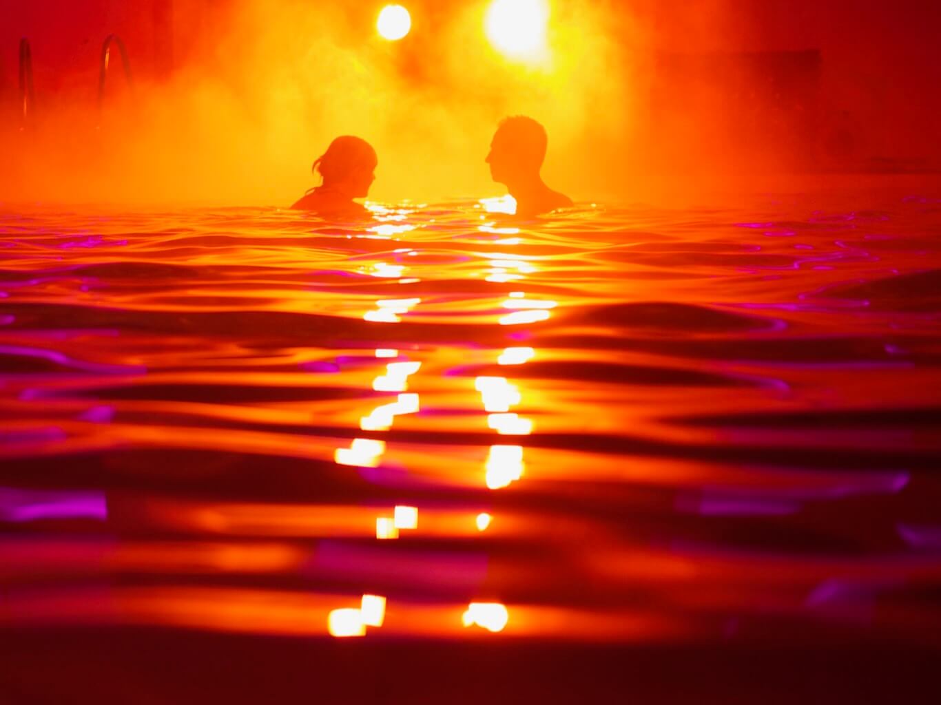 A couple immerses themselves in a swimming pool that has been transformed to look like a sunset.