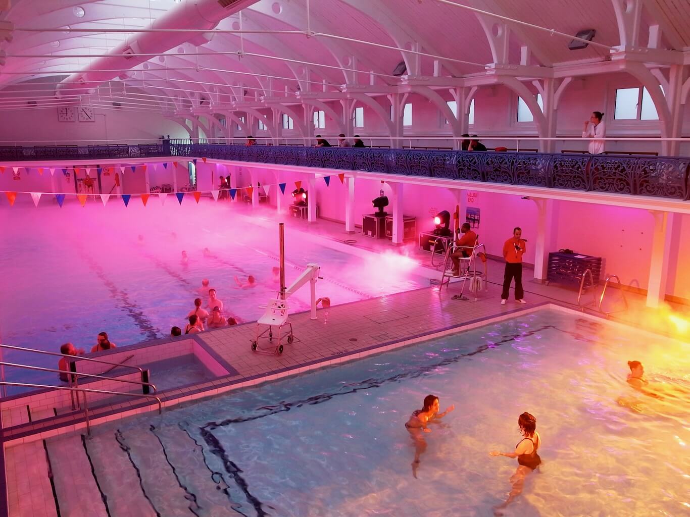 A large swimming pool is illuminated with colourful spotlights and enjoyed by participants.