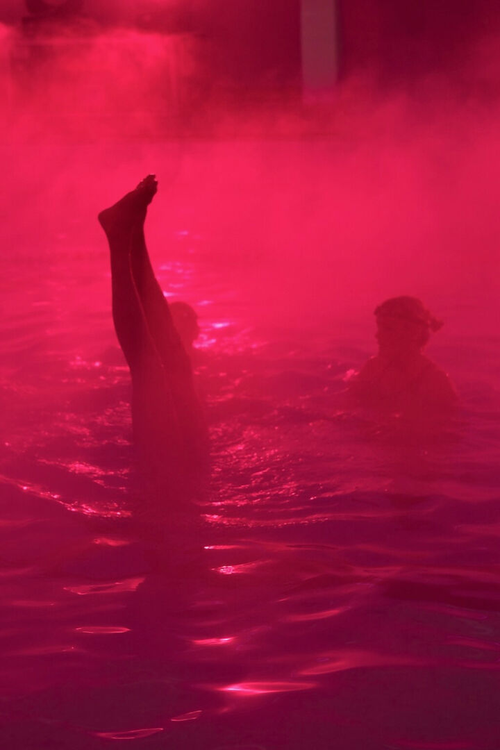 A pair of legs disappear into a pink pool of light, fog, and water.
