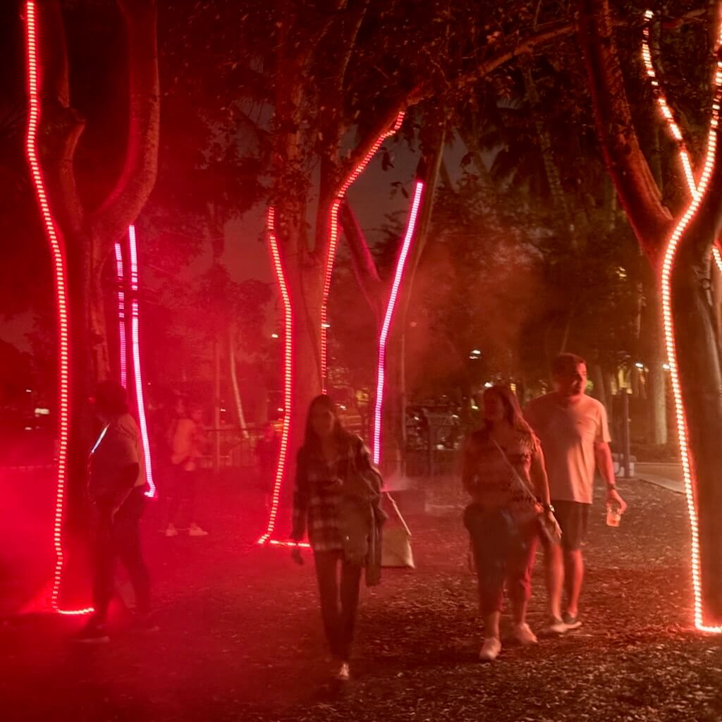Four members of the public stroll through a forest illuminated in shades of red.