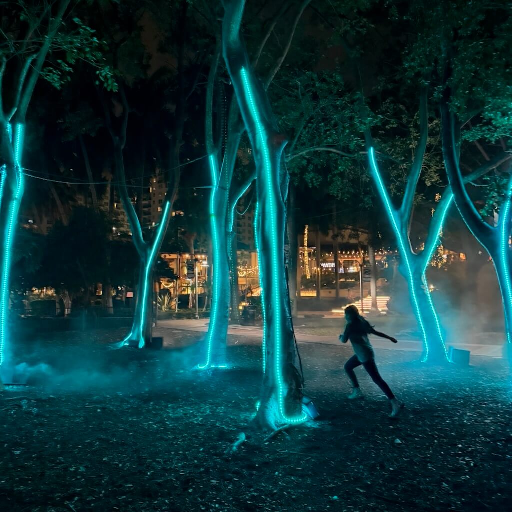 A girl runs through woods, surrounded by trees covered in ribbons of cyan light.