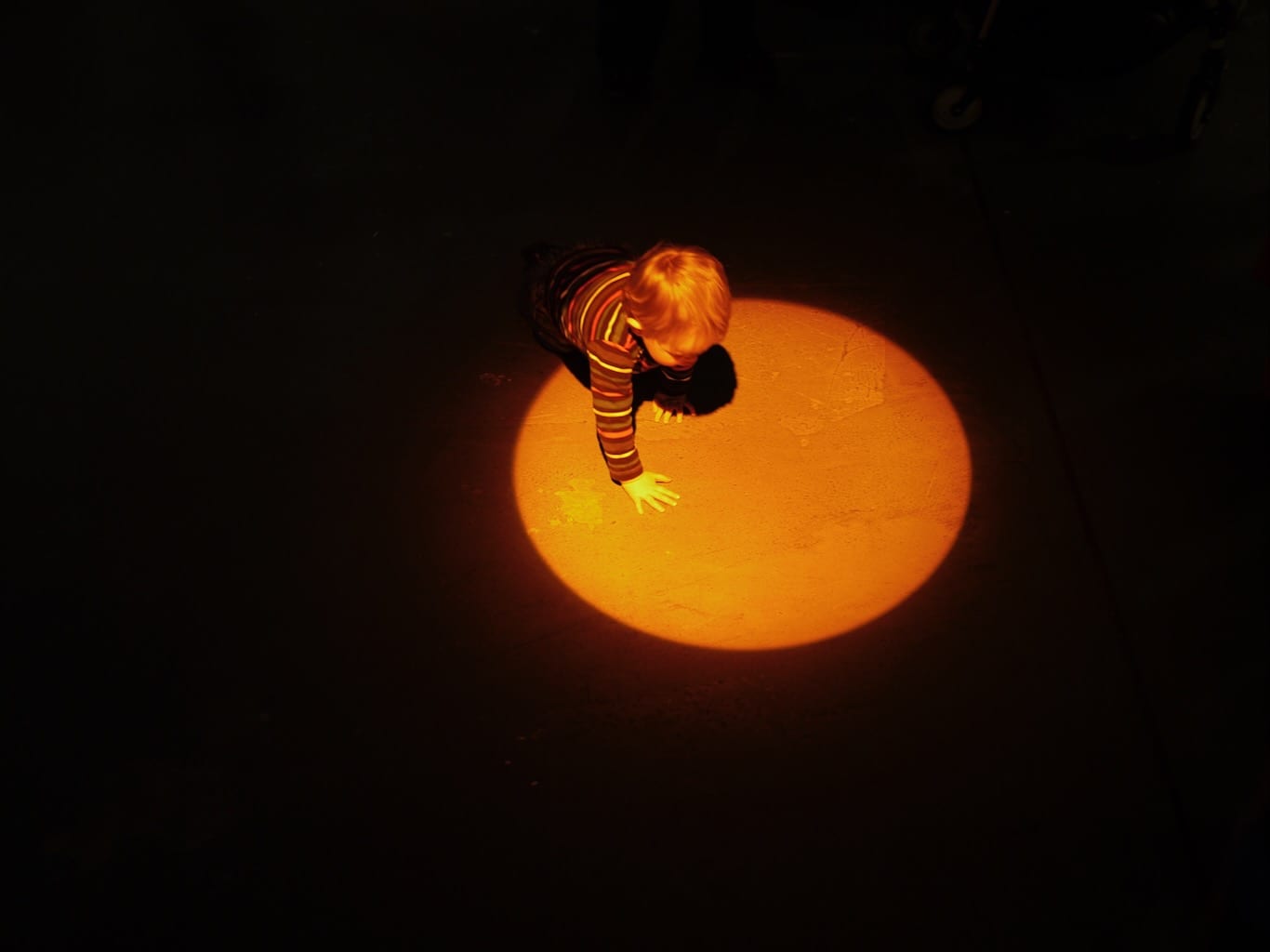 A toddler playfully emerges from darkness into an orange spotlight.
