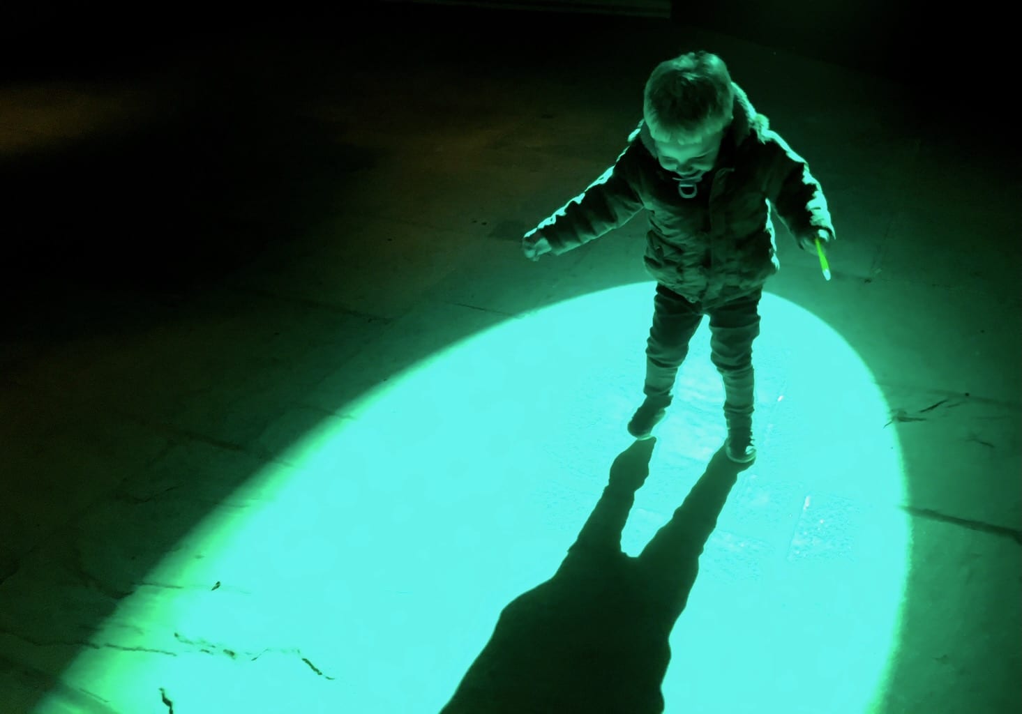 A toddler happily smiles as he plays with a green spotlight.