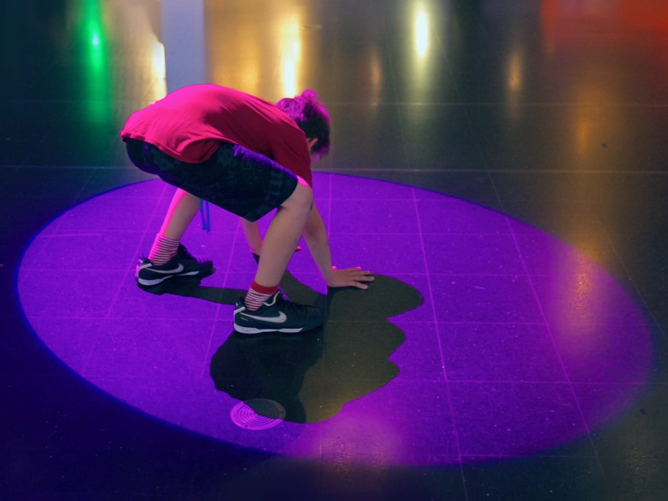 Reaching for the floor, a boy finally catches a purple spotlight.