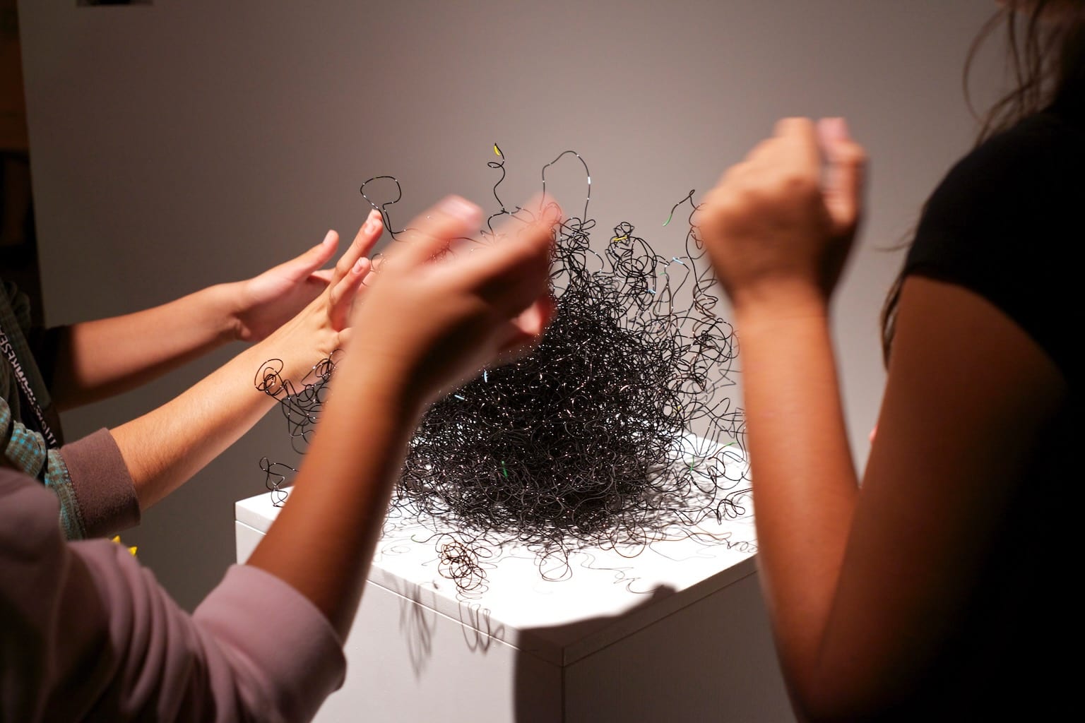 A tactile wire sculpture is playfully activated by people's hands.