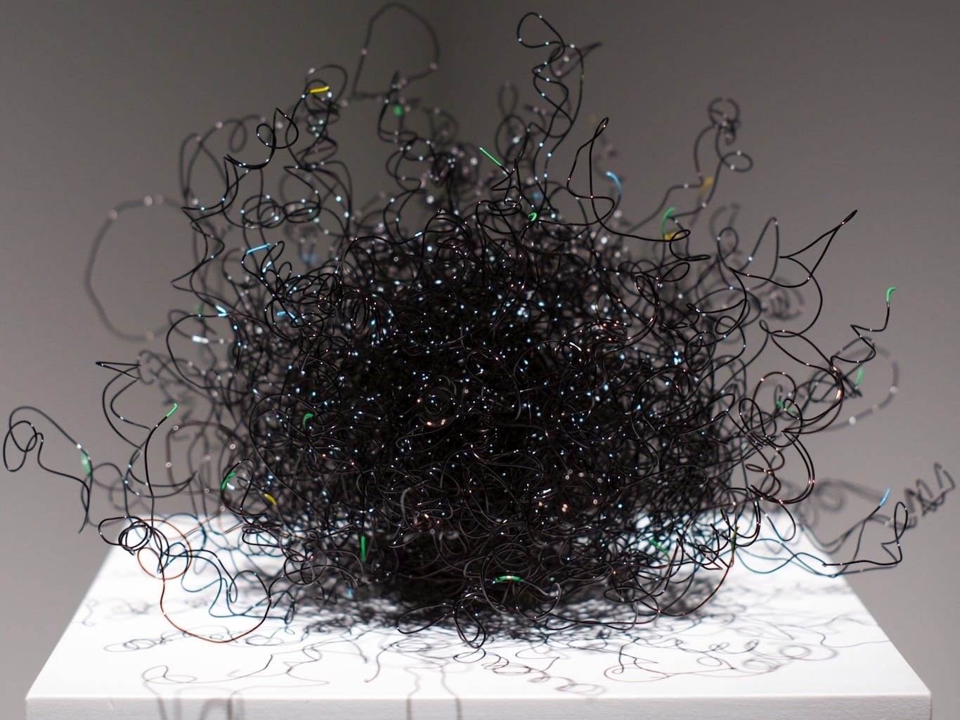 Echidna, a sculpted wire ball creates sits atop a podium in a spotlight, invites onlookers to play with it.