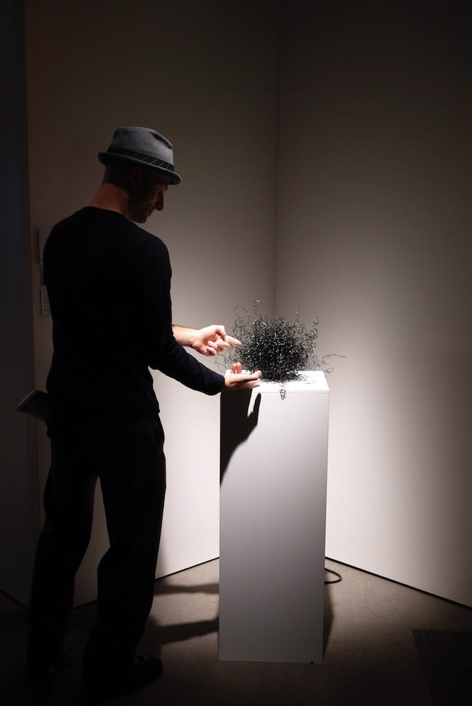 Spotlighted on its podium, Echdina the wire sculpture is activated by a man playing with strands of wire.