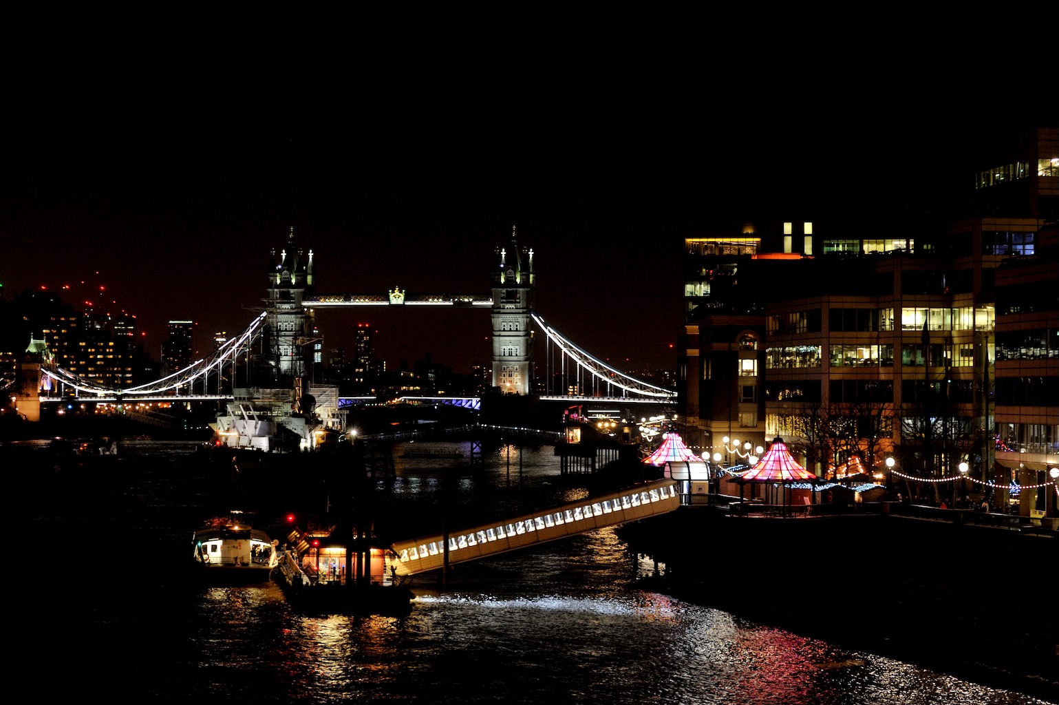 London Bridge sits over the river Thames, framed by two beautifully lit pavilions in shades of peach.