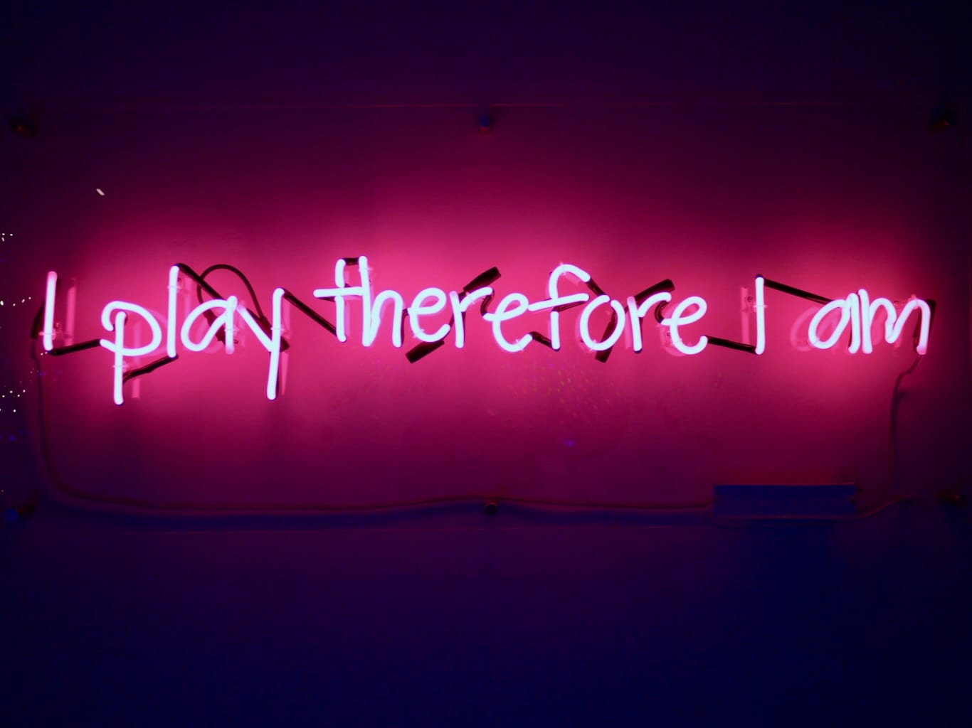 The foundation of Tine's work is captured in a bright pink neon sign reading 'I play therefore I am'.