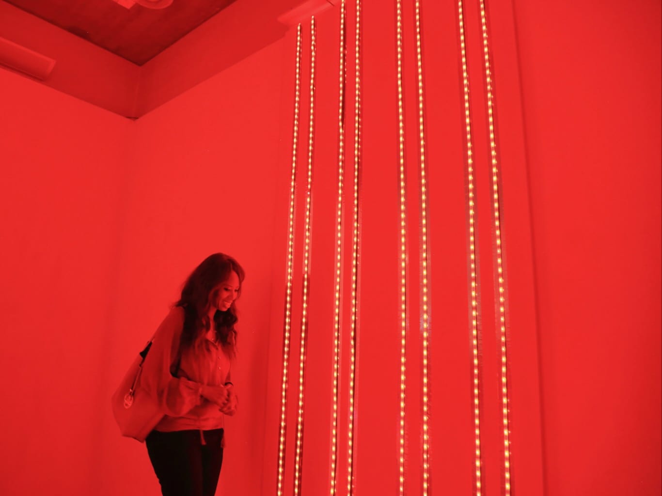 Bright red lights trail from floor to ceiling as a woman looks on it awe.