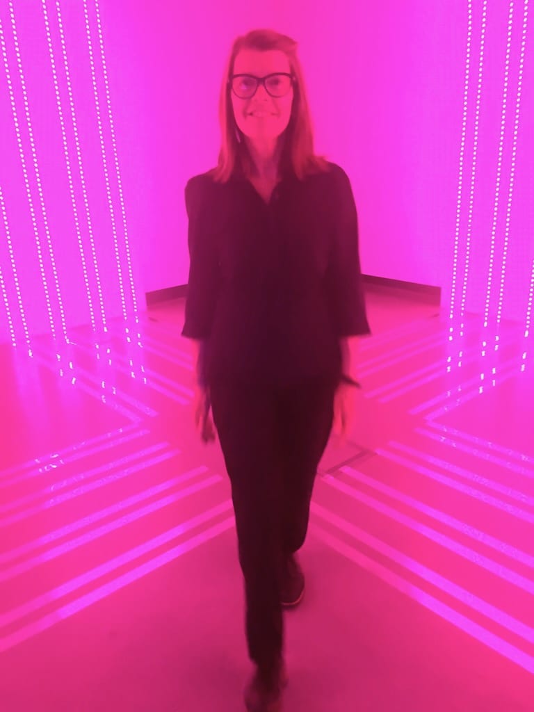 Standing proud, a happy woman poses with the bright pink lights.