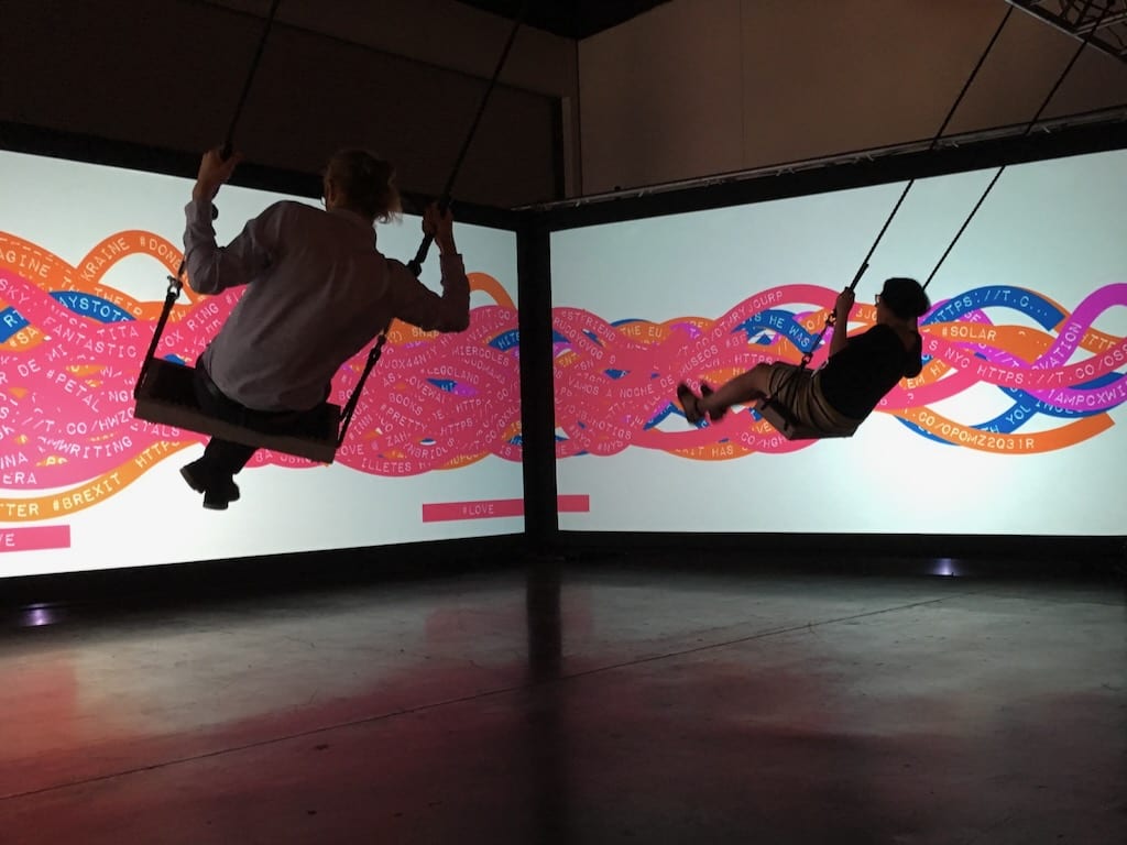 A closeup of 2 participants swinging on Tine's interactive swing set, creating new combinations of colour and words with each movement.