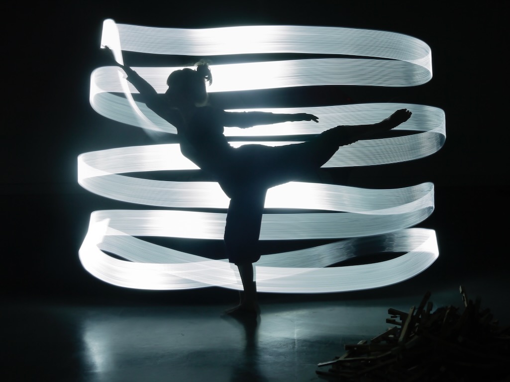 The silhouette of a dancer is illuminated by ribbons of white light.