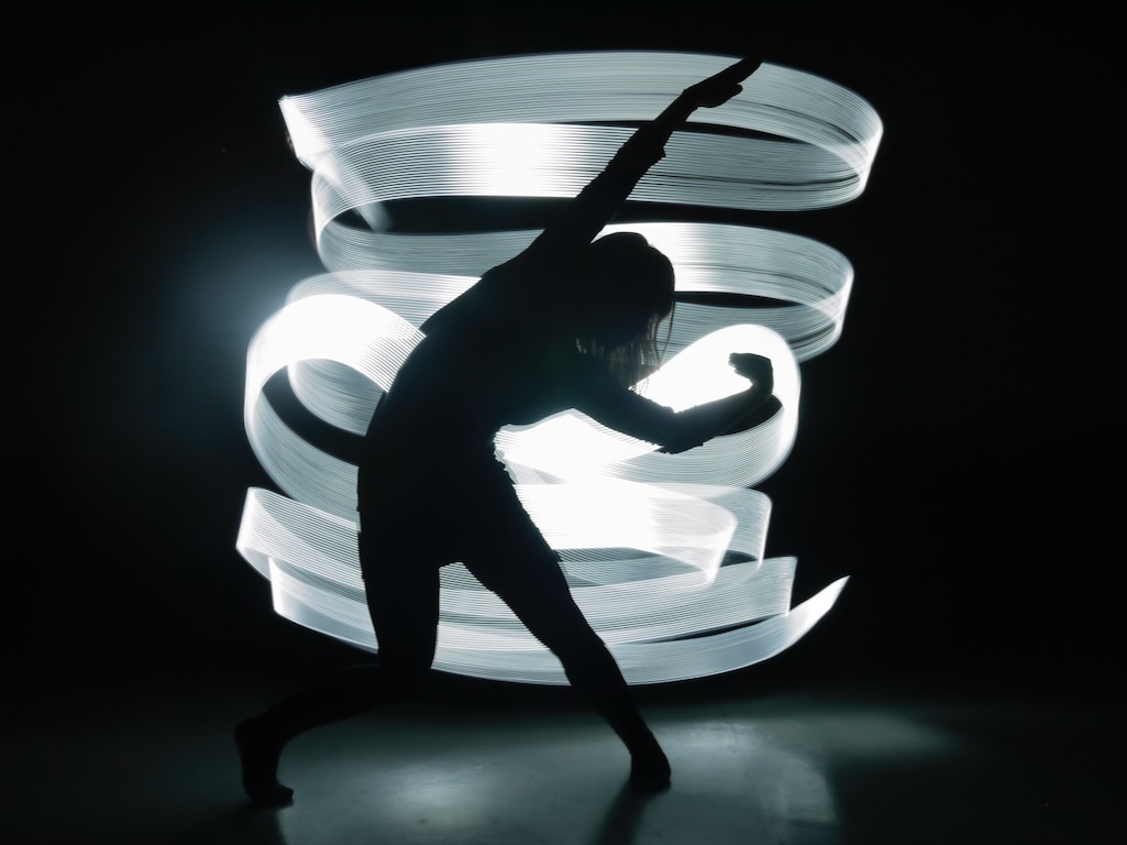 The silhouette of a dancer is illuminated by ribbons of white light.