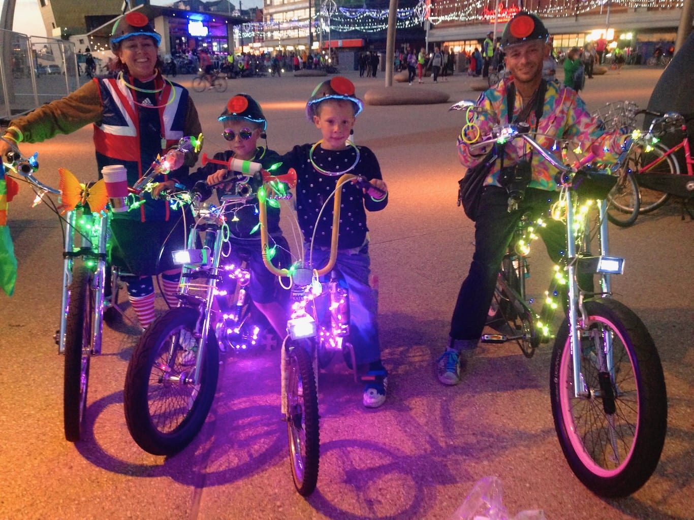 A happy family rides bikes decorated with colourful lights.