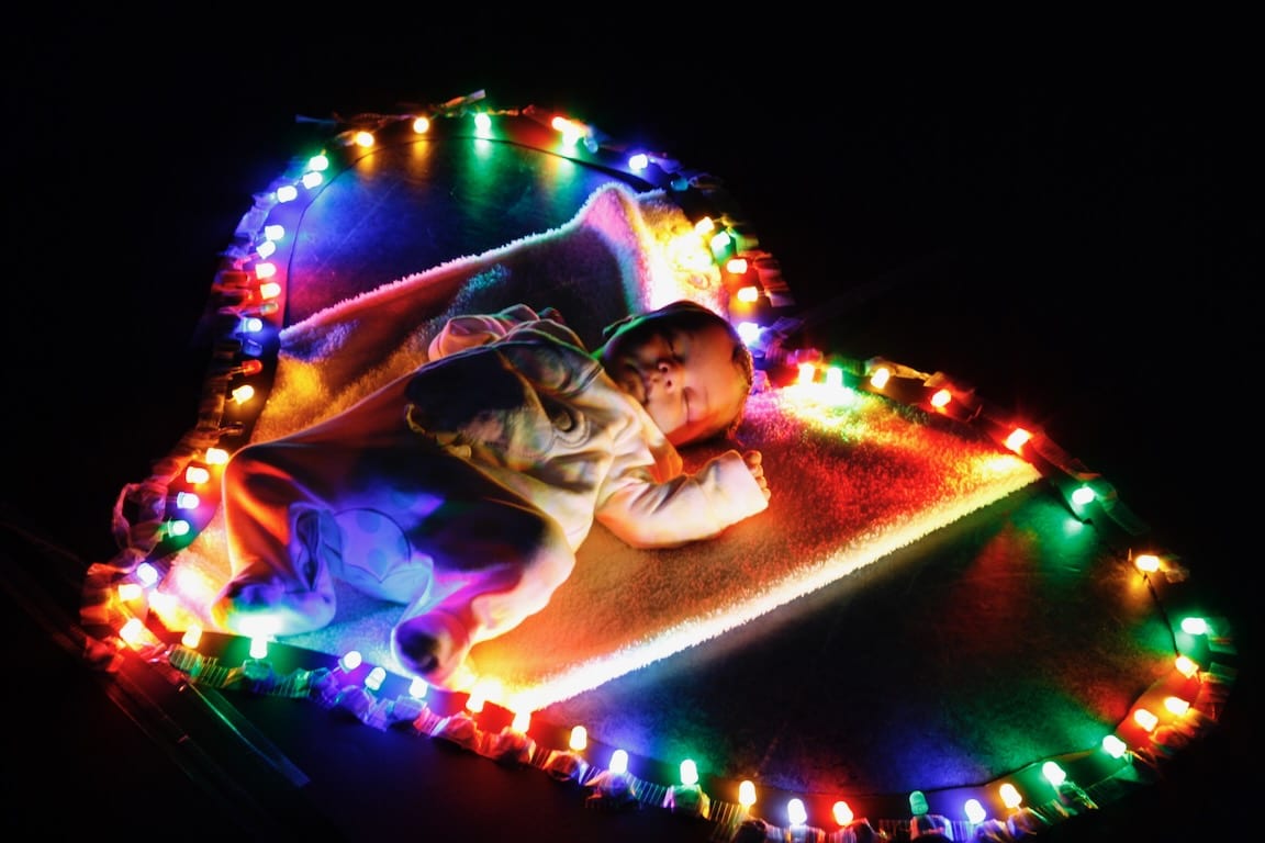 A young baby lays on a blanket inside a heart-shaped string of lights.
