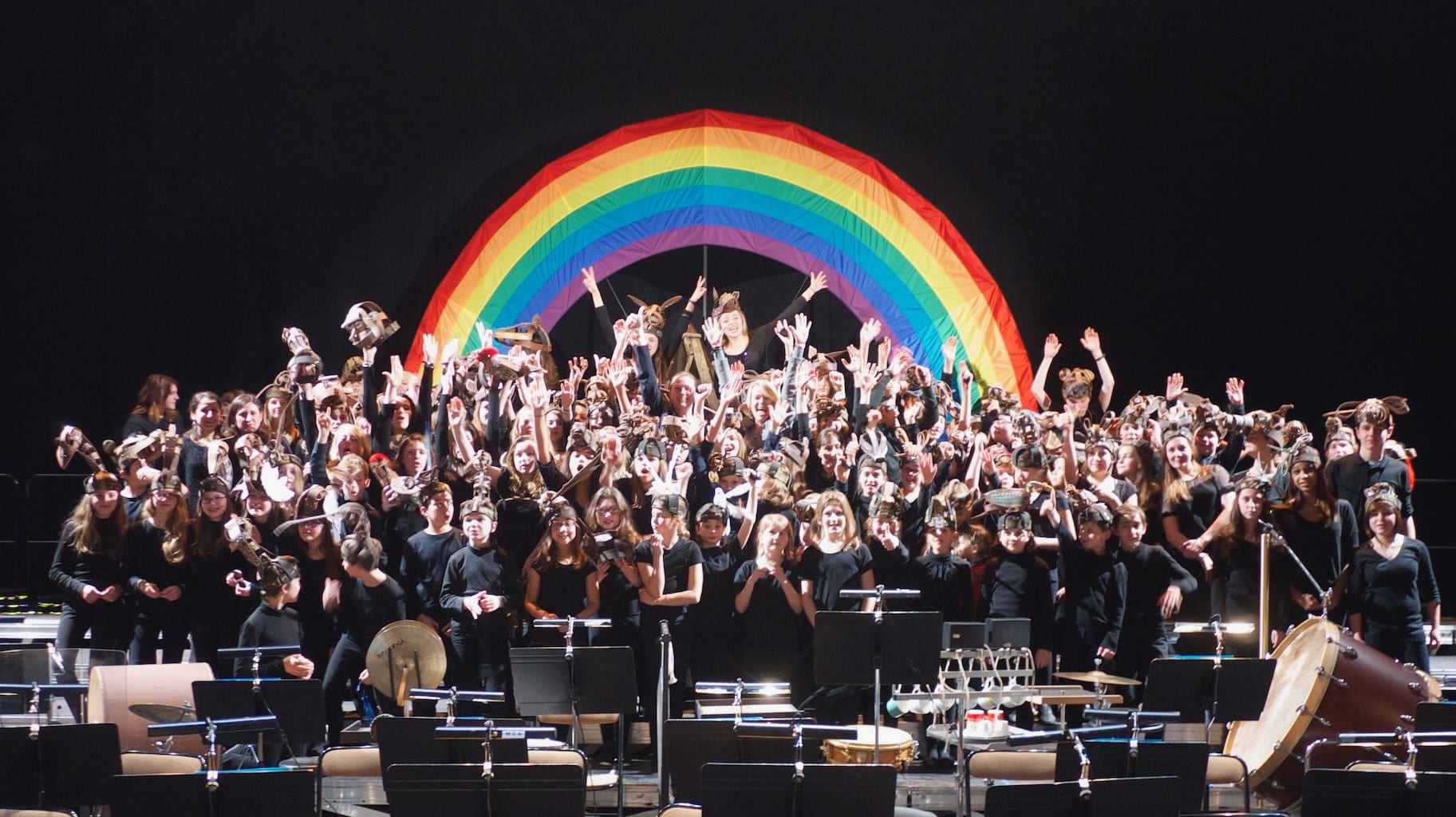 The entire ensemble of Noye's Fludde celebrate their successful performance in front of a rainbow.