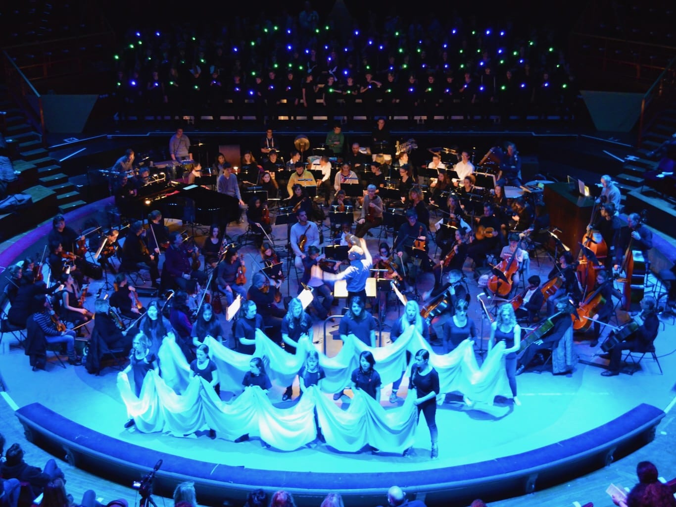 The theatre stage is awash in blue light as dancers create movement with swathes of fabric.