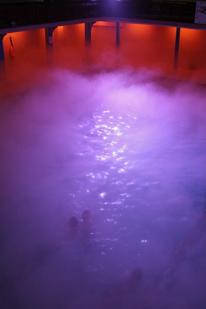 A birds eye view of an ethereal swimming pool illuminated with purple fog.