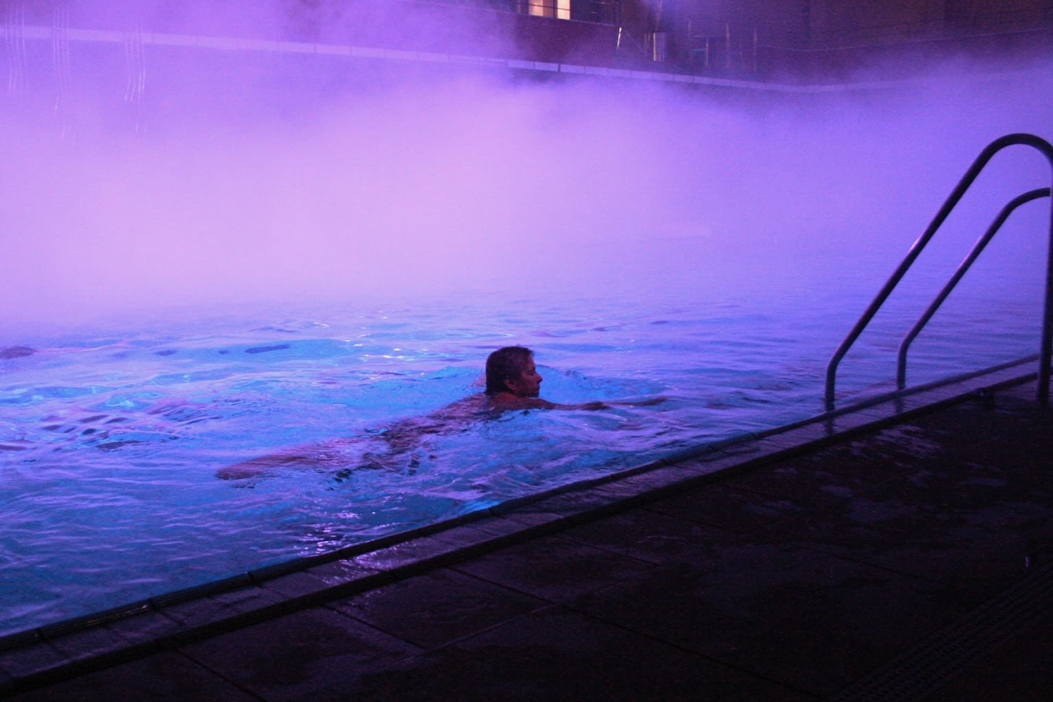 A solitary swimmer glides through a swimming pool awash with bright purple mist.