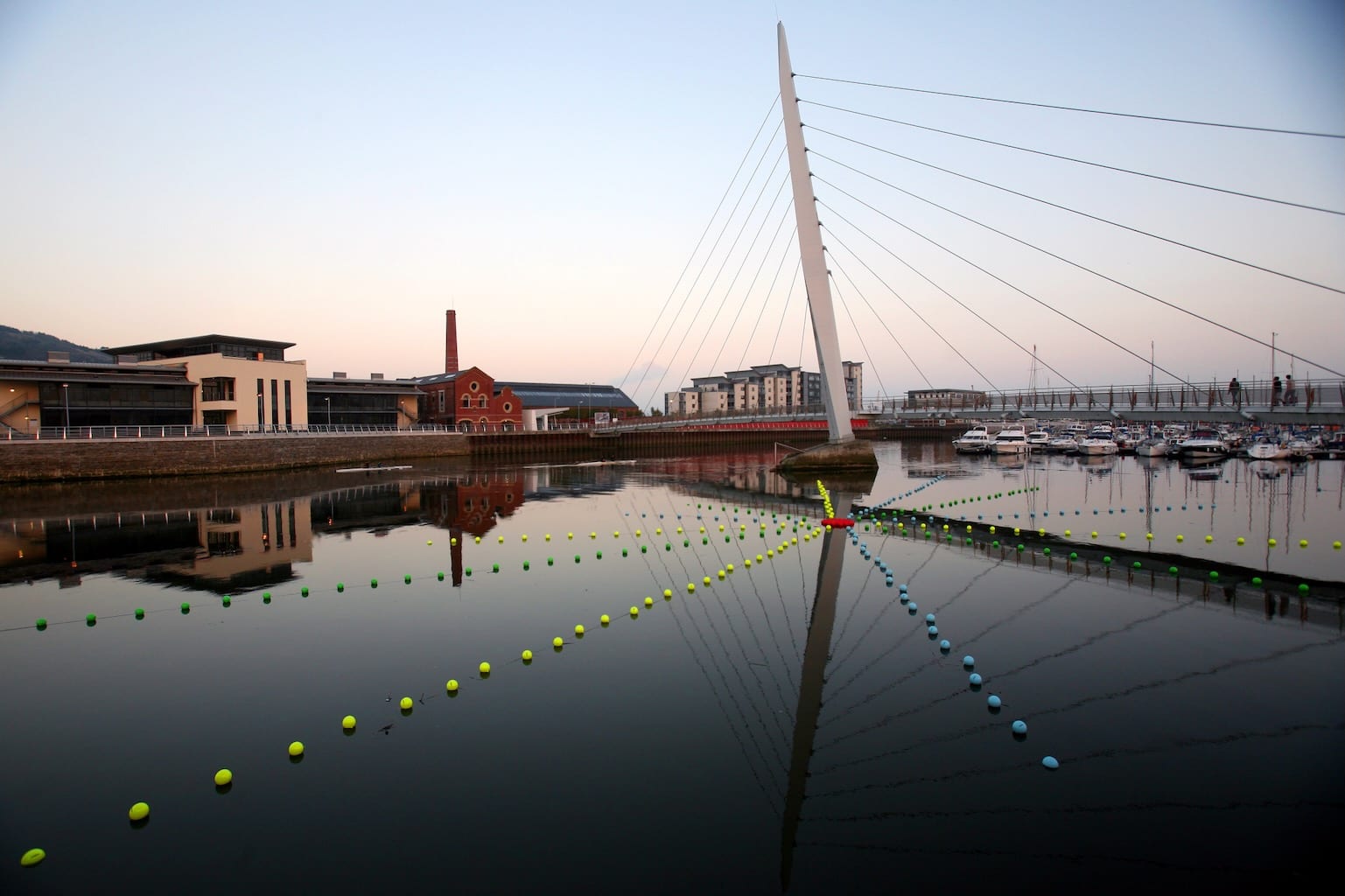 Lines of buoys intersect with the reflection of a bridge, creating a web colour and shapes.
