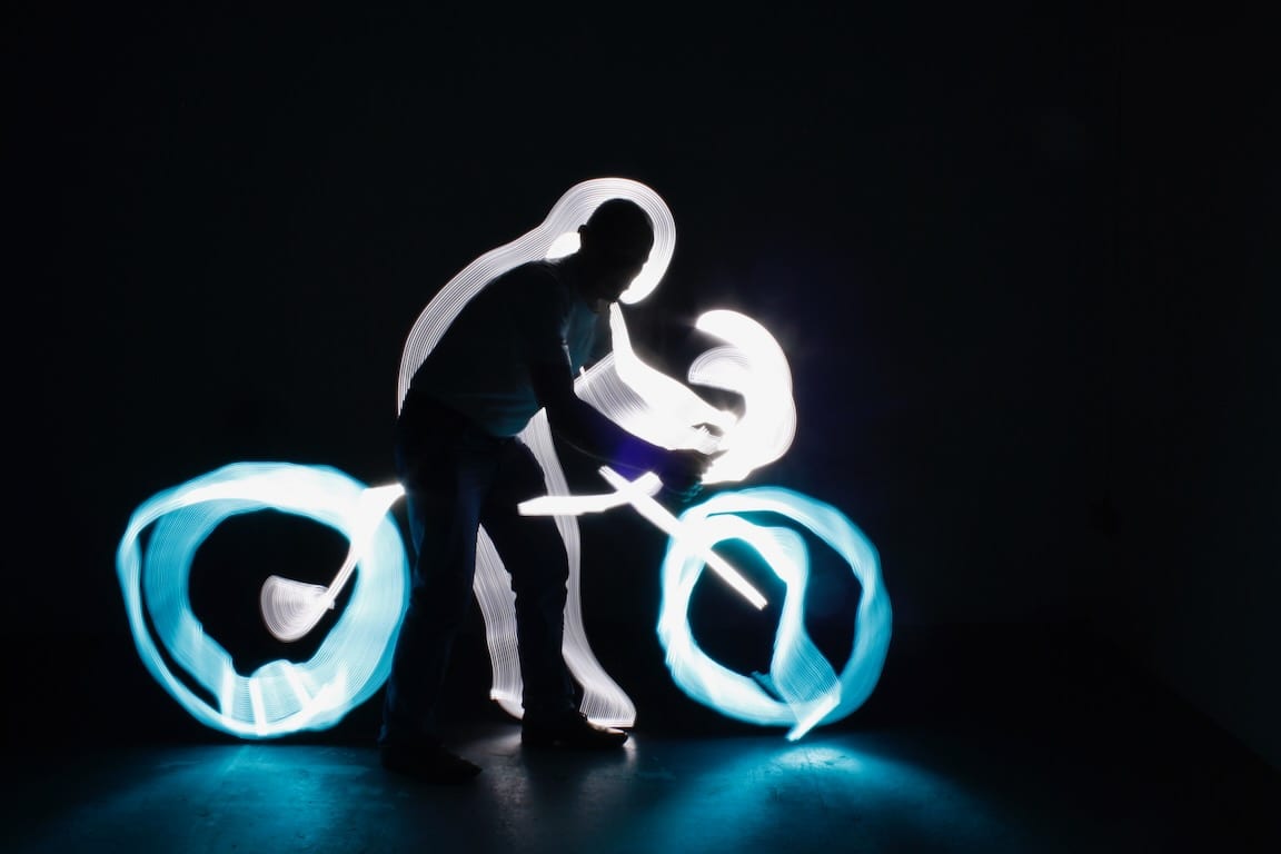 A man's silhouette appears to be riding a bike made of light trails.