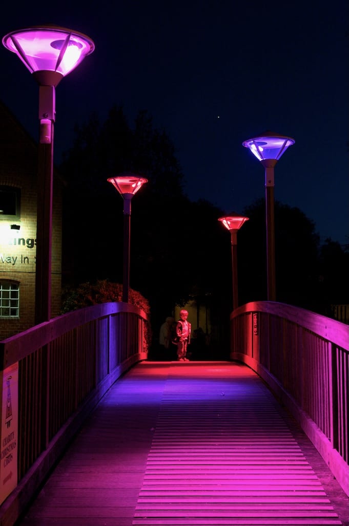 A small boy looks in wonder at a bridge lit up in swathes of pink, blue, and red by Tine's lampposts.
