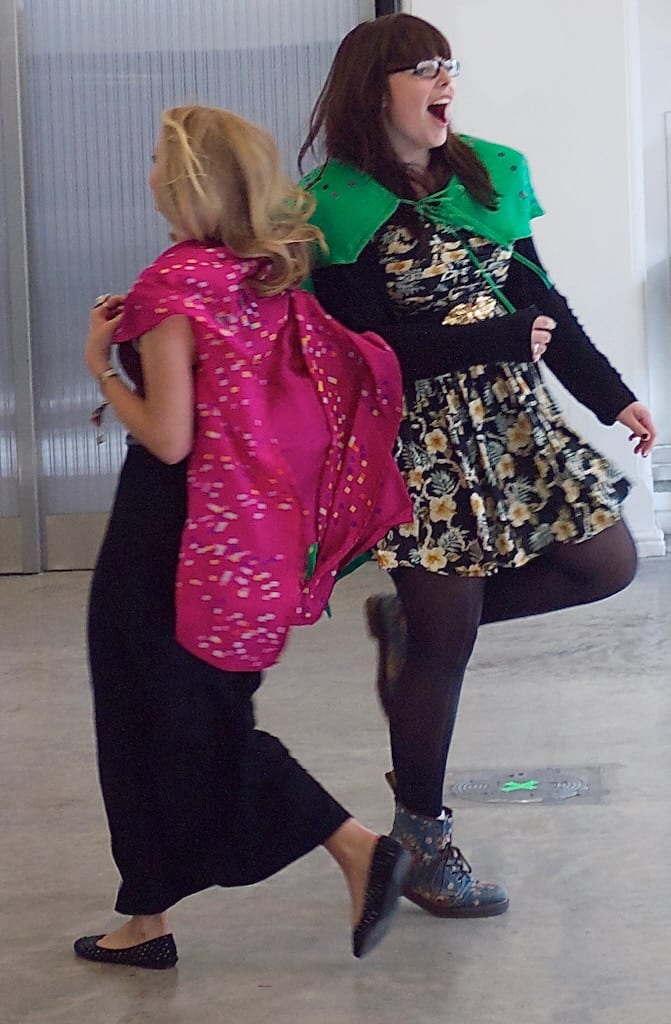 Two women playfully interact in colourful capes, their faces lit up with joy.