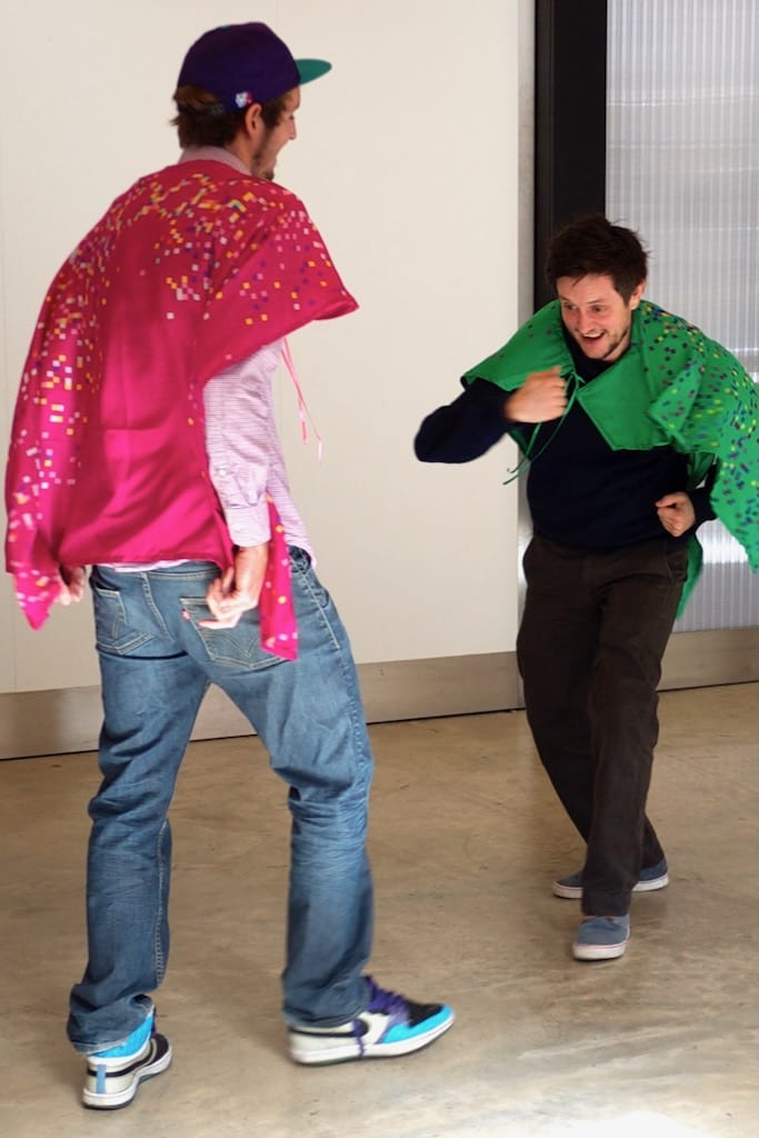 Two men playfully interact in colourful capes.