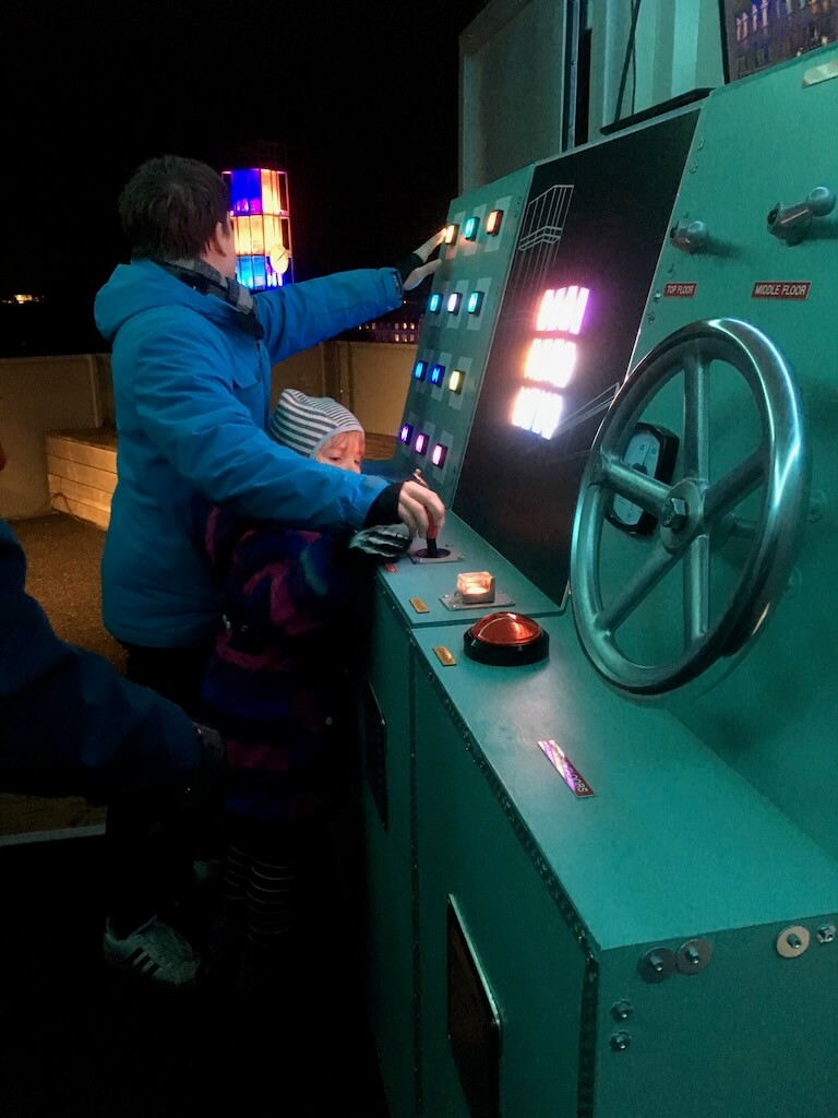 Two kids play with levers and buttons to activate lights in London, from a control room in Denmark.